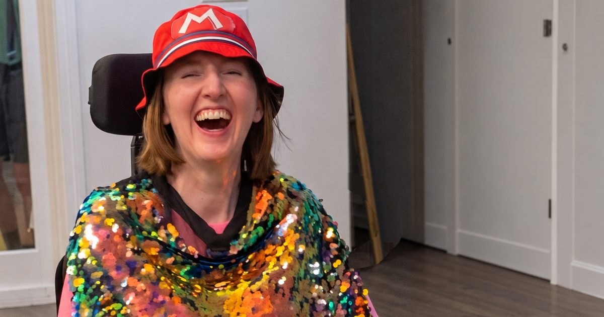Erin Taylor laughing in a red hat and a rainbow sequin wrap