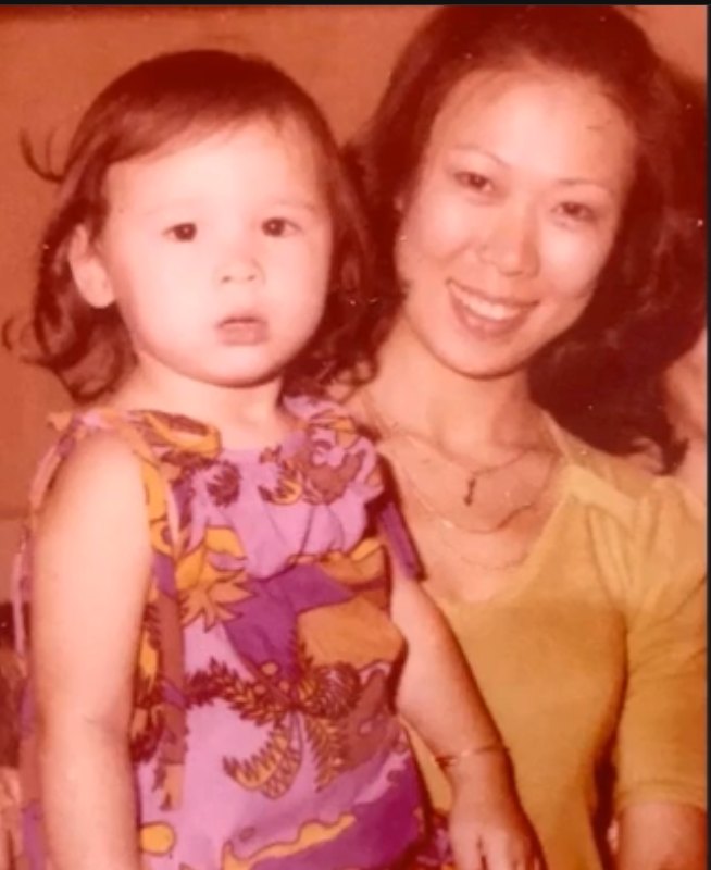 Natasha as a young child in a purple and gold dress, held close by her mother, Margaret Sung